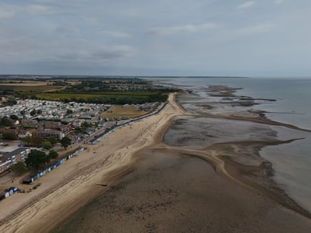 Aerial view of West Mersea beach with a long sandy stretch, beach huts, residential area and tidal flats