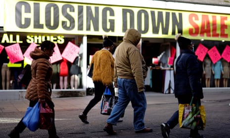 Pedestrians walk past 'closing down sale' signs in the window of a shoe shop
