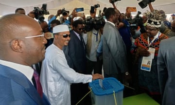 Mahamat Idriss Déby Itno puts a ballot paper in a container surrounded by security staff and people holding up phones and cameras inside a white tent