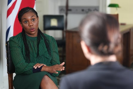 She sits wearing green and black dress and faces interviewer