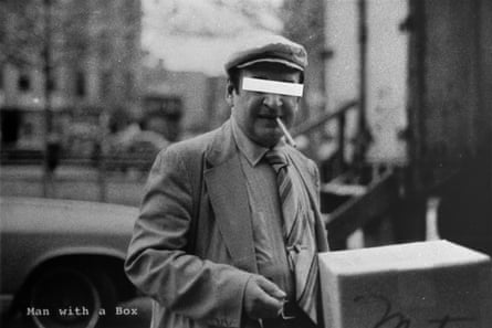 Photograph of a man in jacket and tie and tweed hat, smoking a cigarette and holding a largish cardboard box