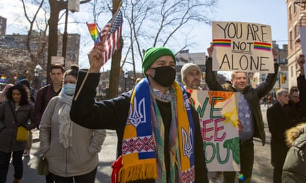 people hold signs saying ‘you are not alone’ and ‘we see you’, with rainbow flags and american flags