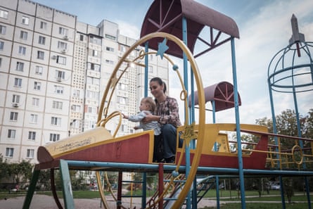 A woman and child in a playground with a tall apartment building in the background