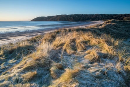 A landscape of grassy dunes, sea and distant wooded hills