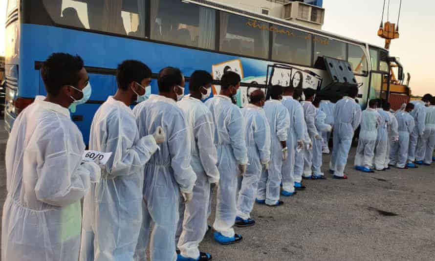 Migrants wearing overalls and face masks are lining up to board a bus after they disembarked from the Mare Ionio vessel in Pozzallo, southern Sicily on 20 June, 2020.