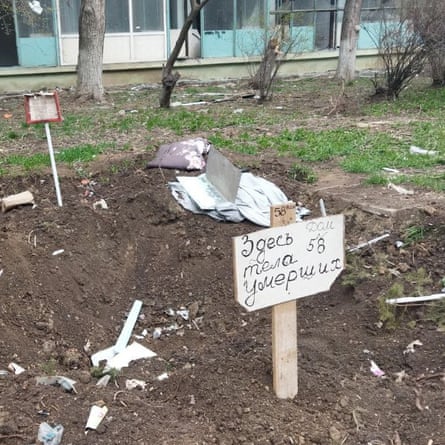 A makeshift grave in a courtyard, with a grave marker reading: ‘Here lie the dead bodies from apartment building 58.’
