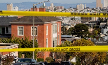 Taken from the top of a hill, with the hills of Oakland far in the distance, a three-story brick house on a corner, with yellow police tape in the blurred foreground.