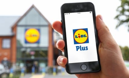 A man uses the Lidl Plus App on his phone outside a Lidi Store in the UK