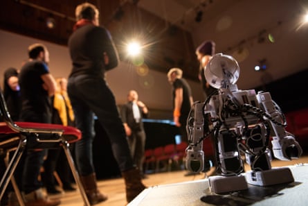 A toy robot in the foreground with a standing audience behind