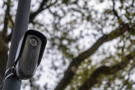 A surveillance camera mounted on a pole near some trees.