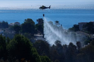 Water is sprayed from a helicopter on to a forest. The sea is visible in the distance