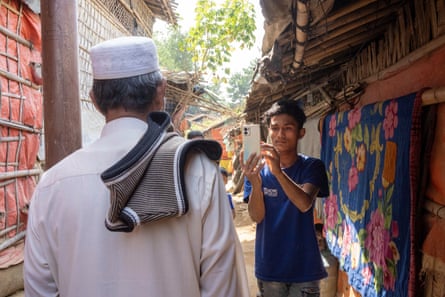 An older man stands with his back to the camera as a boy takes his picture with a mobile phone