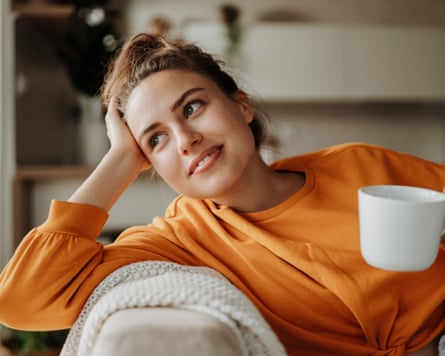 Young woman resting on sofa with blanket and cup of tea.