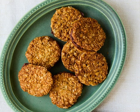 Anzac sandwich biscuits with dark chocolate filling on green and pink plates