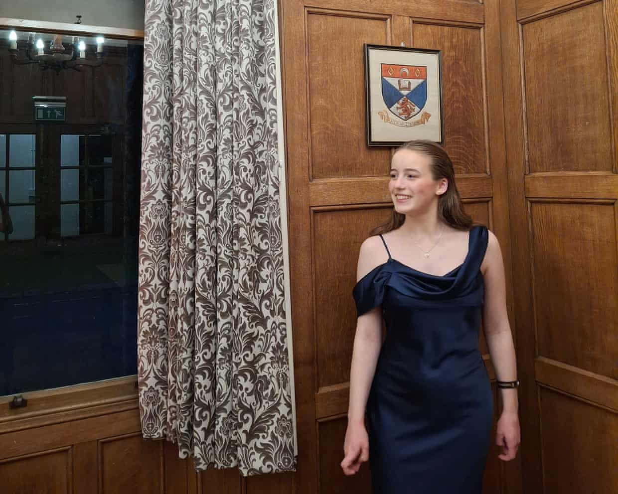Sophie Rose Jenkins in black dress by window with university crest above on wood panelling