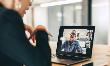 A business woman is speaking during a virtual meeting with coworkers on a screen. The laptop is sitting on top a wooden table