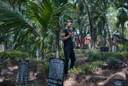 مردی در حال خواندن نماز مسلمانان در مقابل قبر در میان درختان خرما 
