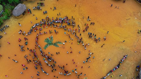 An aerial view of lines of people standing in an open space around an arrangement of palm fronds