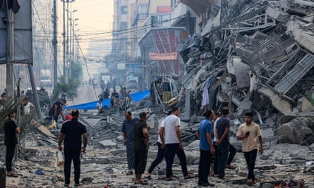 People walking in a debris-strewn street next to a collapsed building