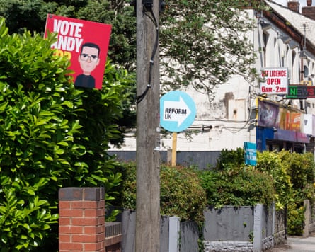 Placards for Andy Burnham of Labour and Robert Kenyon of Reform UK in adjoining front gardens.