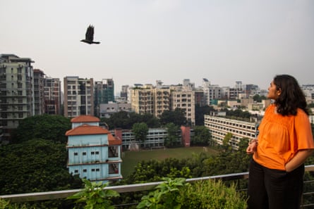 امرأة شابة على السطح تراقب طائرًا يطير أمامها، على خلفية أبراج المدينة