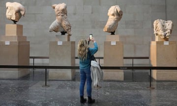 A woman takes photographs with her mobile phone of sculptures in a museum.