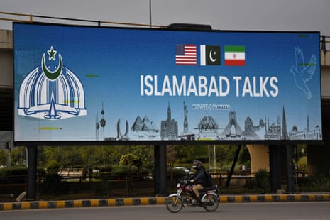 A man rides a motorbike past a billboard with the message "Islamabad Talks".