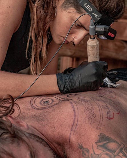 woman leans over someone’s back with tattoo needle
