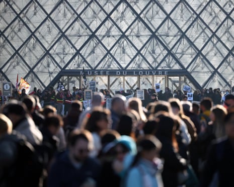 Protesters gather with signs and flags outside the Louvre Museum's glass pyramid entrance