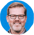 man in glasses smiles with blue background