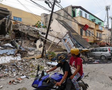 Two motorcyclists look at a devastated building.