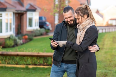 Happy couple looking at smartphone while standing in front yard