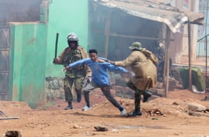 A riot police officer grabs a young man by the collar of his long-sleeved top as another office holds a truncheon alongside