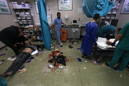 Doctors and nurses treat patients on a ward. Blood is spattered over the floor and one patient is being treated on the floor without a bed.