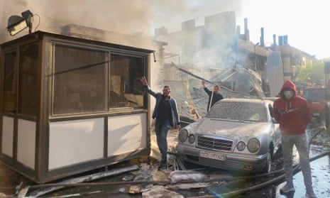 Smoke rises as people gesture at the damaged site.