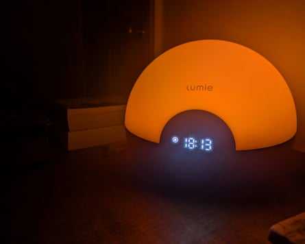 A Lumie Bodyclock Glow 150, glowing orange, on a nightstand