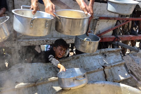 A Palestinian boy extends an empty pot in front of a charity kitchen to receive cooked rice, in Gaza City.