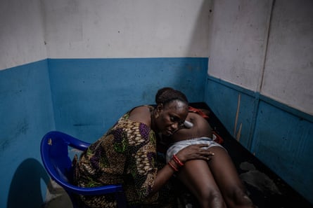 A black woman wearing an Ankara African print dress uses a tube to listen to a pregnant woman’s stomach