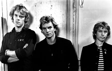 A black and white photograph of three men in dark clothing standing in a line in front of a wall, looking serious.