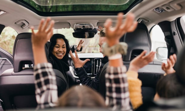 Cheerful family raising hands while enjoying road trip in electric carPosed by models GettyImages-1252669239