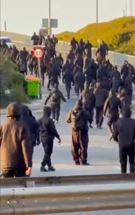 Men in black hoodies and balaclavas mass on a road in a demonstration