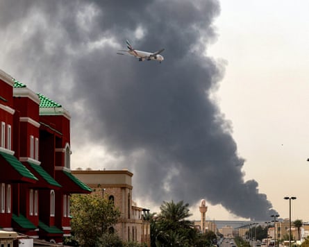 An Emirates aircraft prepares for landing as smoke rises from a fire near Dubai international airport.