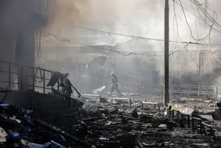 A rescue worker walks across rubble at a shopping centre with smoke behind him
