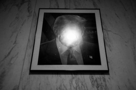 A framed portrait of Donald Trump obscured by the flare of a ceiling light