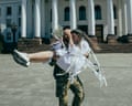 Newlyweds Oleksandr carries Tetiana, laughing, in a plaza with a colonnaded building