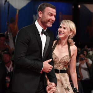 A man in a tuxedo and a woman in an evening gown pose together on the red carpet