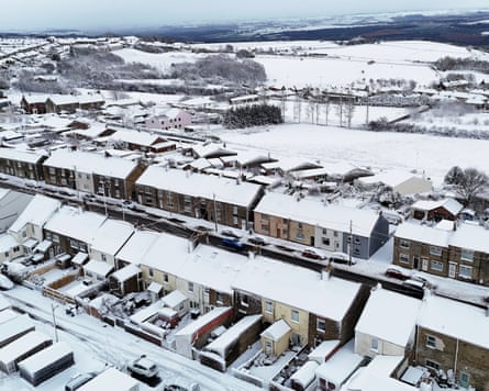 Aerial view of snow-covered roofs in a residential area with fields in the background