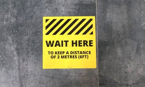 A ‘Wait Here’ social distancing sign sticker on the floor of a coffee shop