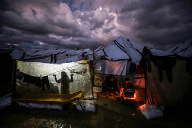 Under a stormy sky, displaced Palestinians cook over a fire