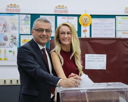 A man and a woman pose for the cameras as they hold ballot papers above a ballot box as they cast their votes.